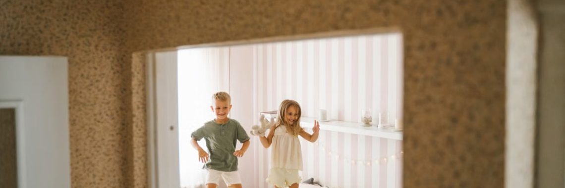Two happy children jumping on a bed in a cozy and cheerful bedroom setting.